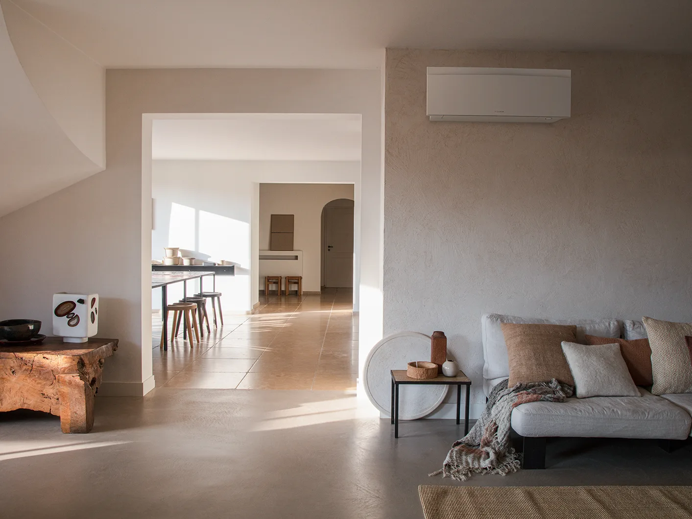 Daikin Emura i matt hvit på en pusset vegg over en lin-sofa i et varmt, solfylt oppholdsrom